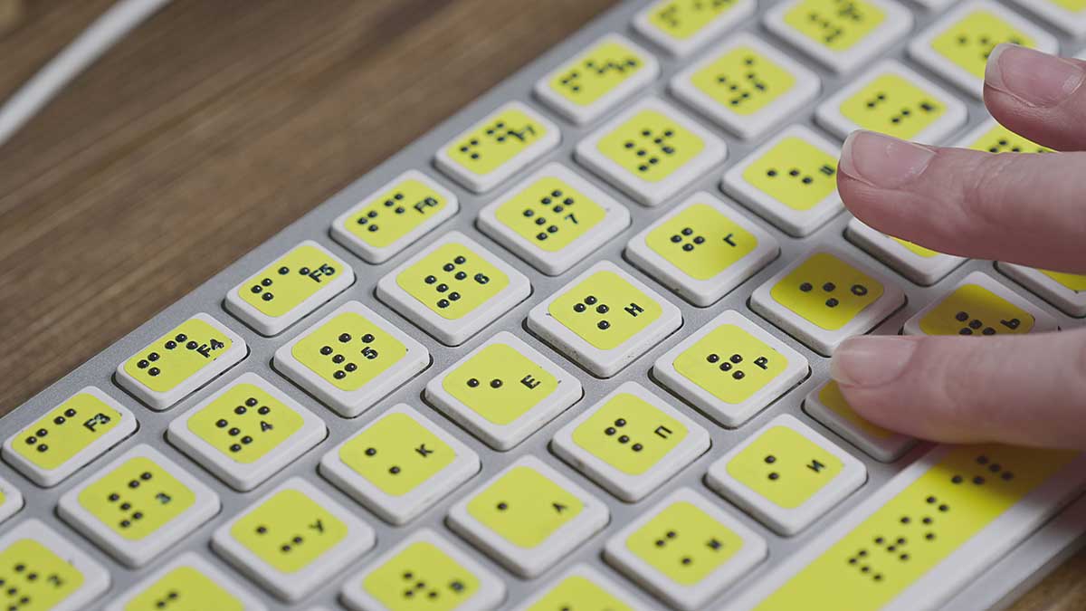 Barrierefreiheit-Tastatur-Braille Finger auf einer Tastatur mit gelben Braille-Aufklebern