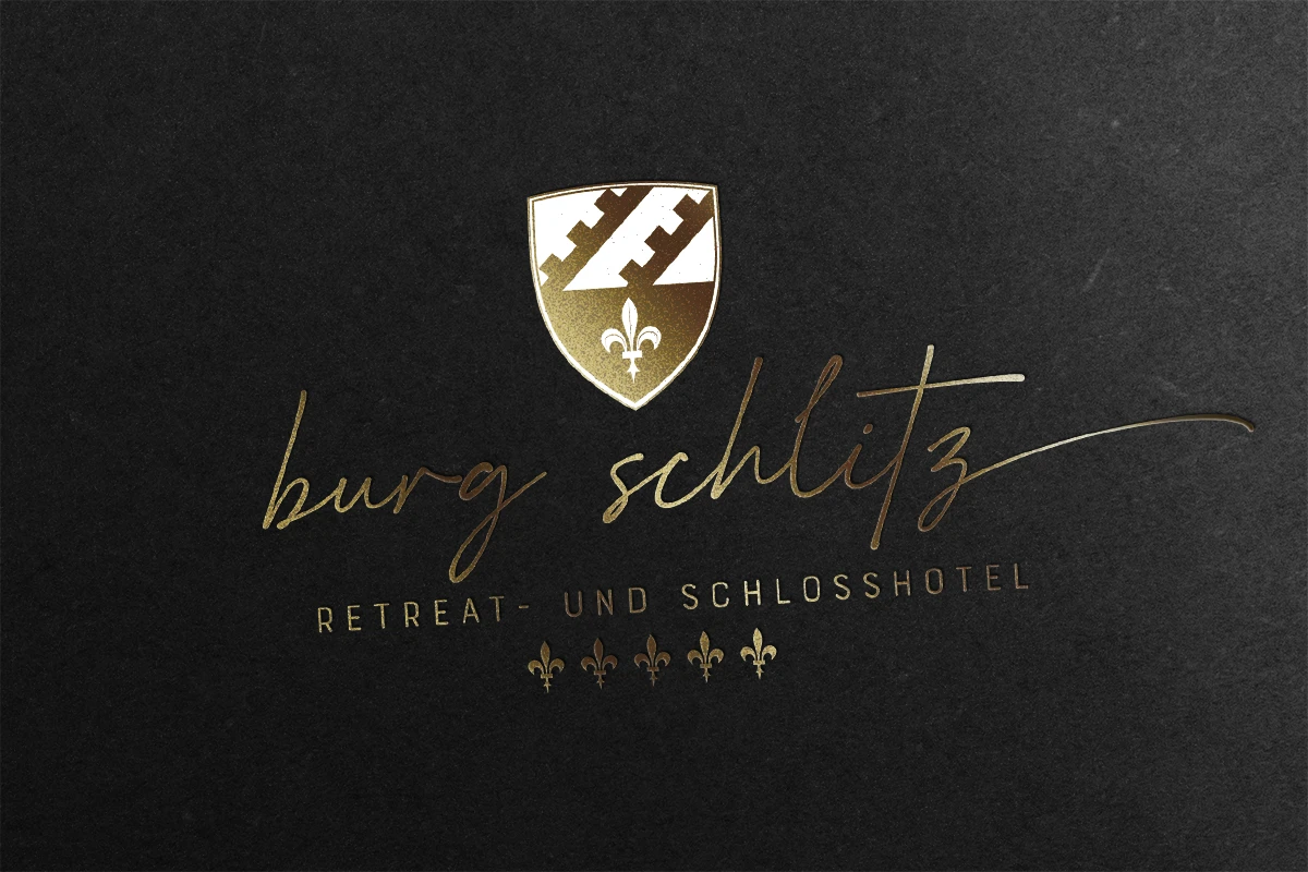 burg-schlitz-hotel-retreat-logogestaltung Goldfarbenes Logo mit Schild, Lilien und Text auf Schwarz - perfekt für einen Corporate Design Relaunch.