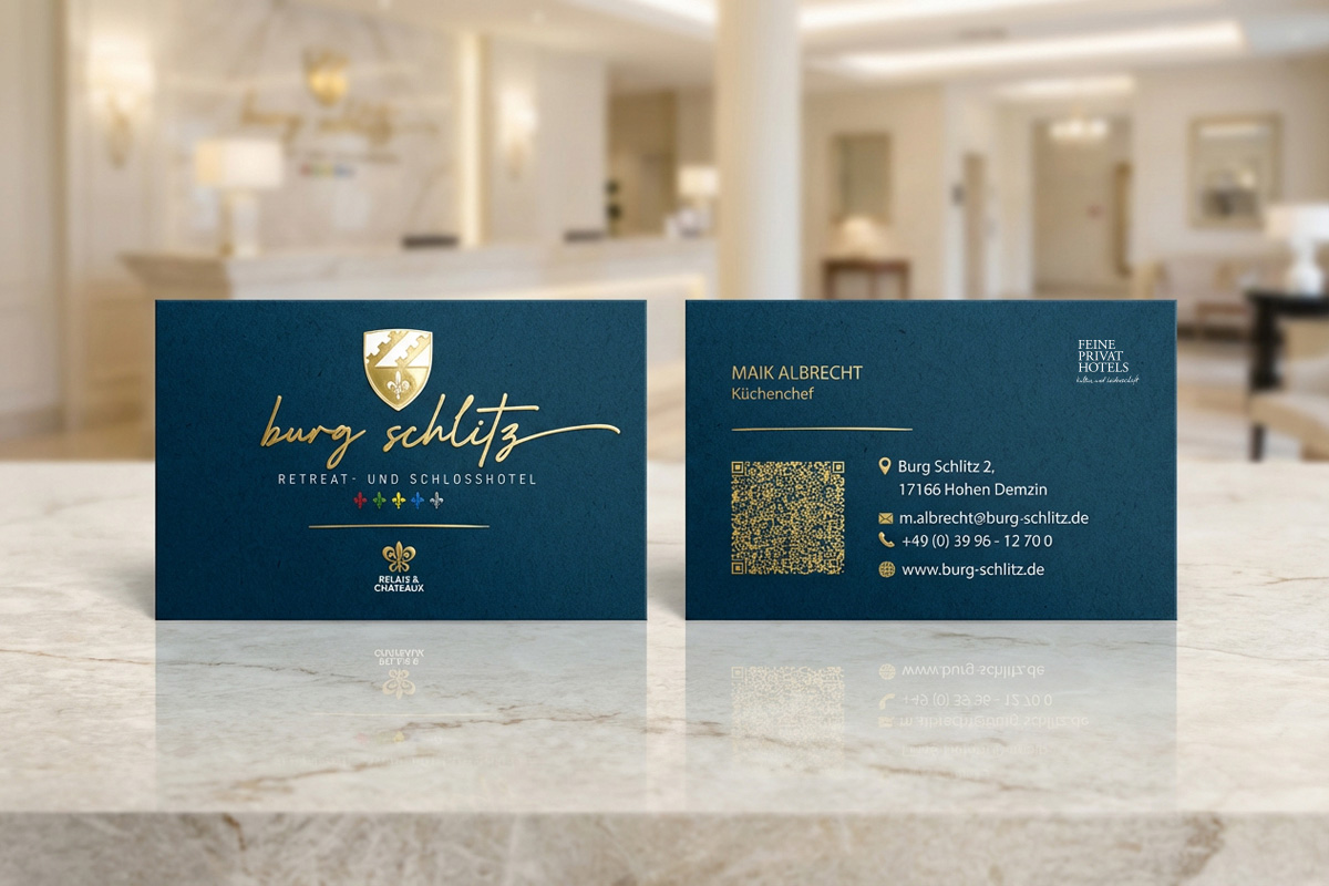 burg-schlitz-visitenkarten Zwei elegante marineblaue Visitenkarten aus dem Corporate Design Relaunch werden in einer hellen Lobby auf Marmor ausgestellt.